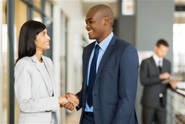 Indian woman shakes hands with African American man in business setting.