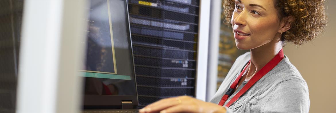 Woman works in a server room with her laptop and server racks.