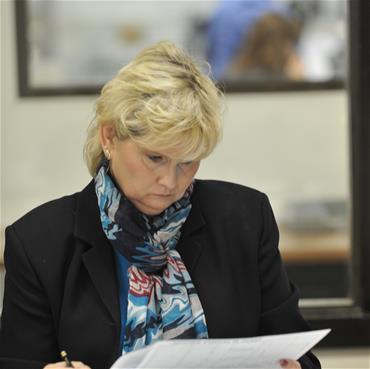 A woman (Rita) works at a desk with paperwork.